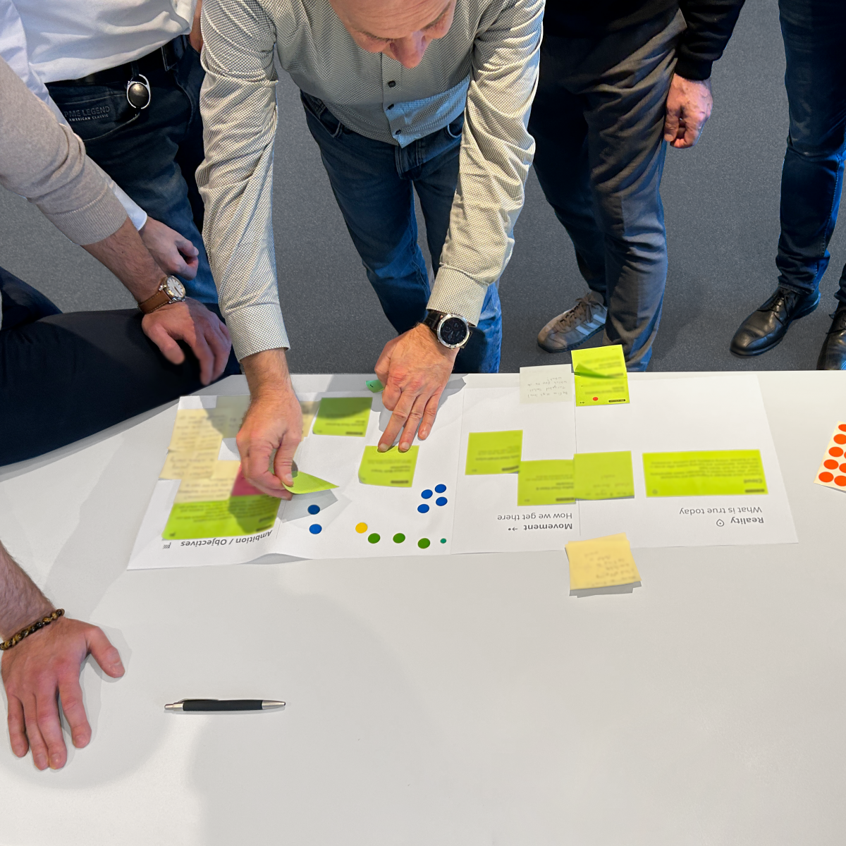 Several people stand around a worksheet and sort Post-Its.