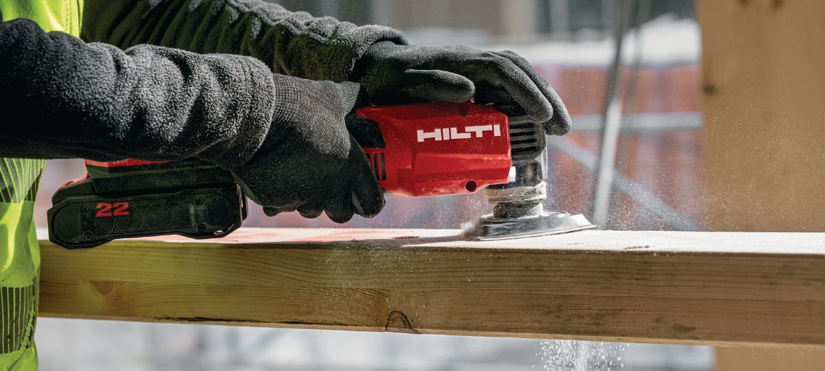 Wooden beam is sanded down using Hilti's multi-tool, sending wood chips flying.